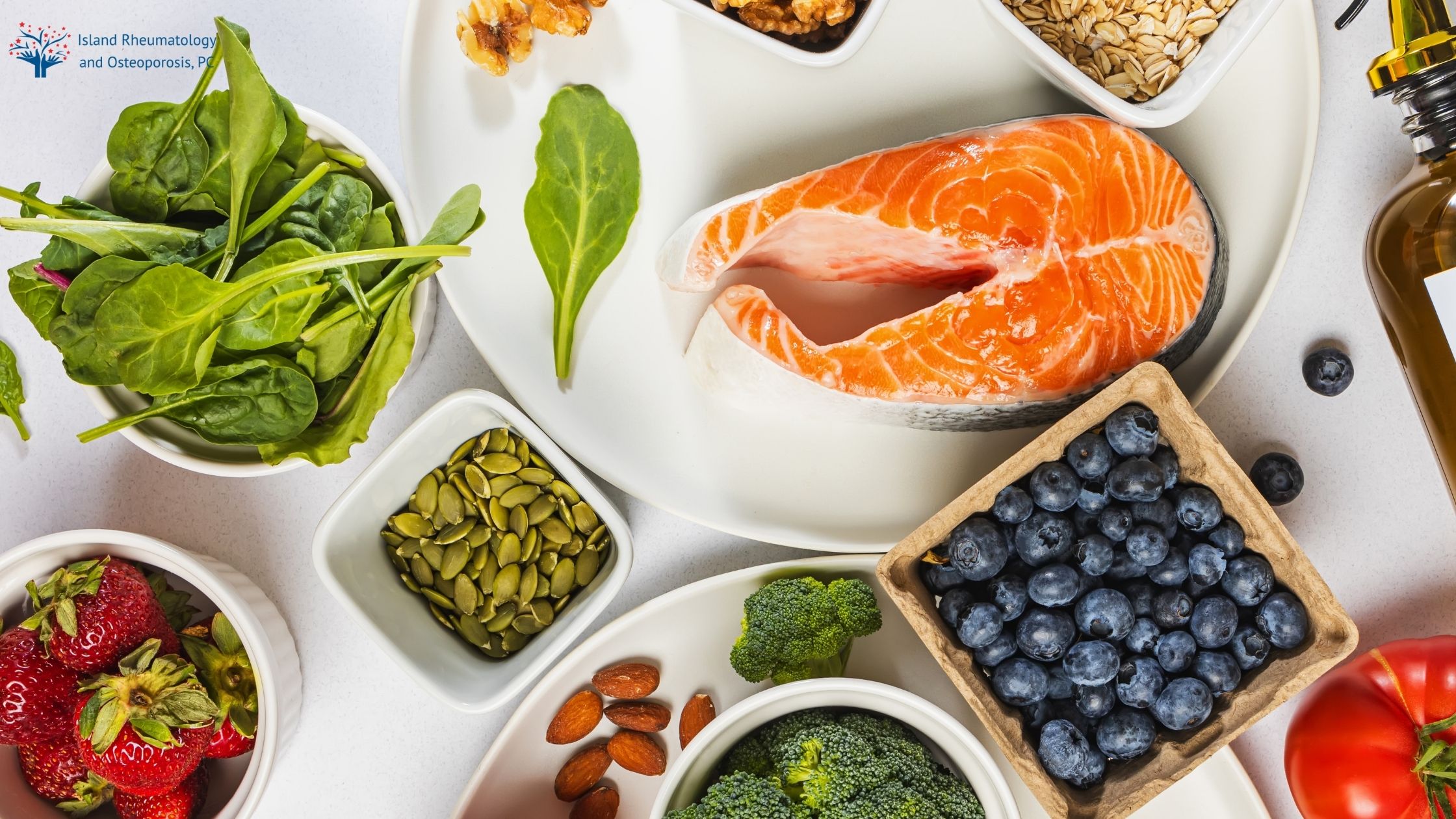 A variety of healthy foods including salmon, blueberries, spinach, nuts, seeds, strawberries, broccoli, and oats arranged on a white surface.